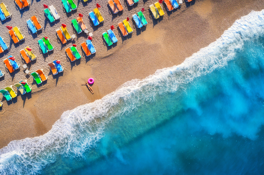 Gdzie na wakacje we wrześniu? Najlepsze kierunki na jesień 51 Kobieta z dmuchanym kółkiem na plaży w otoczeniu pustych leżaków.